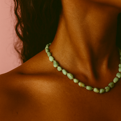 Close-up of a person wearing a green beaded necklace against a pink background