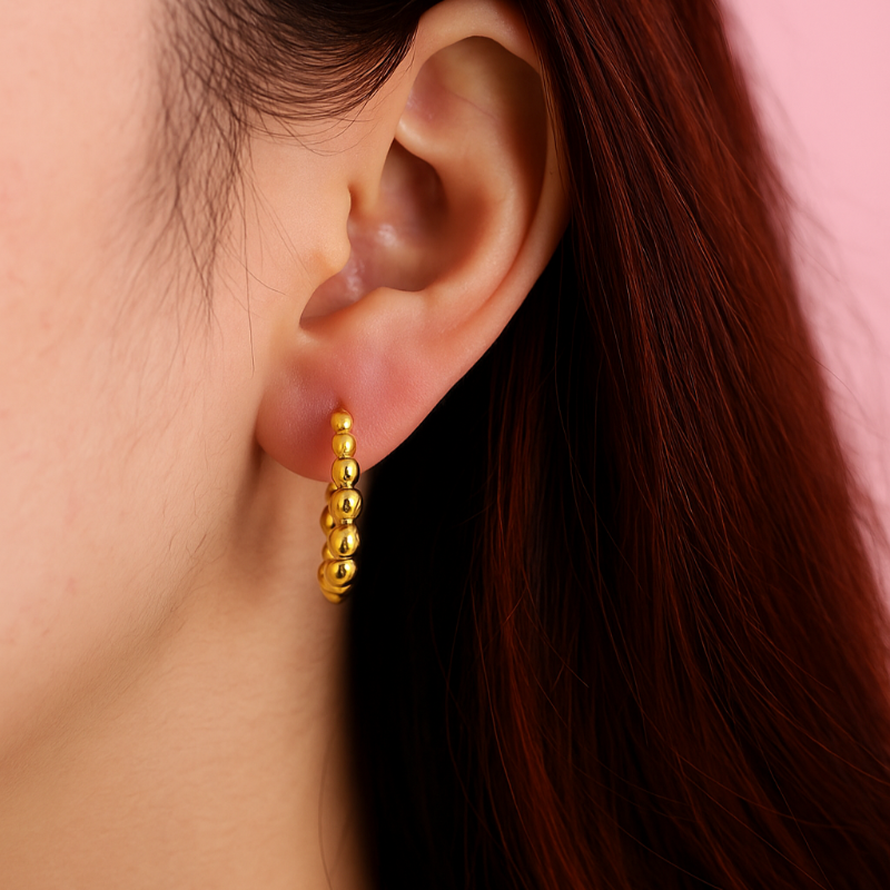 Gold hoop earring worn by a person with red hair against a pink background