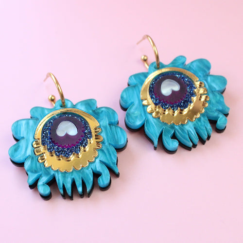 Turquoise earrings with gold and purple centers on a pink background