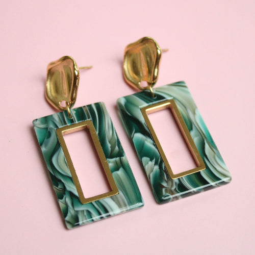Green marbleized earrings with gold accents on a pink background