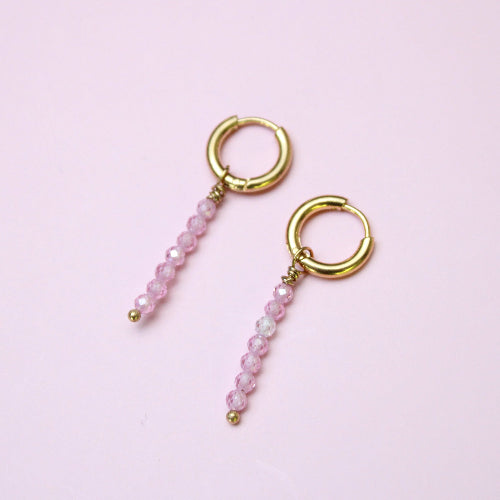 Pair of gold hoop earrings with pink beaded chains on a light pink background
