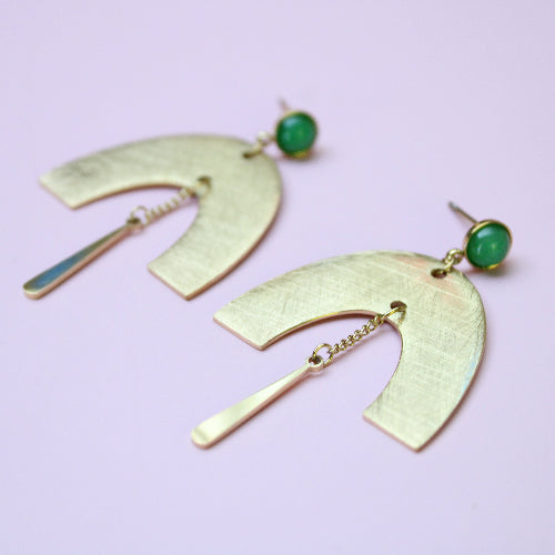 Gold earrings with green gemstones on a light purple background