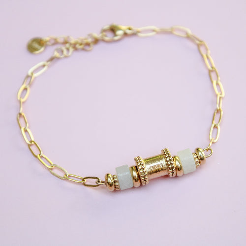 Gold bracelet with white beads on a light pink background