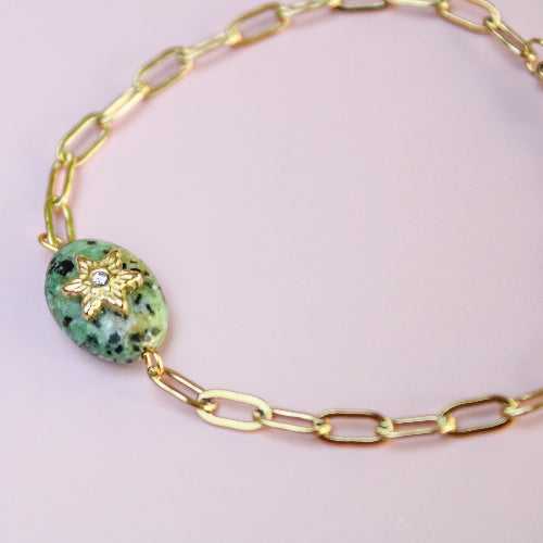 Gold bracelet with a greenstone bead on a light pink background