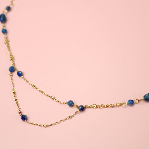 Gold necklace with blue beads on a pink background