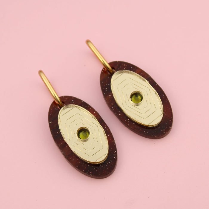Pair of earrings with gold and brown design on a pink background