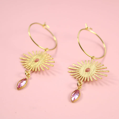 Gold earrings with pink gemstones on a pink background