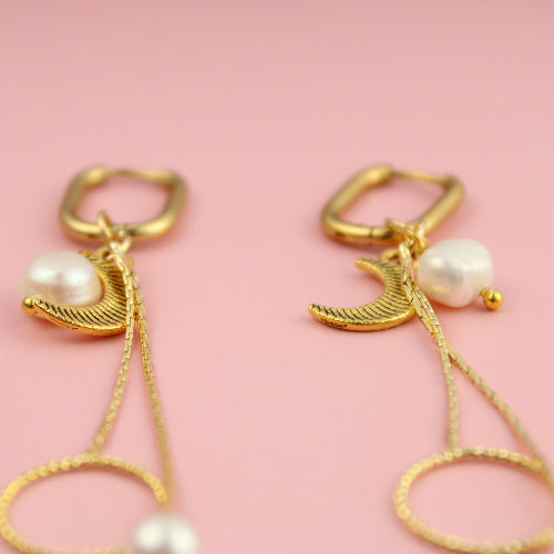 Gold earrings with pearl drops on a pink background