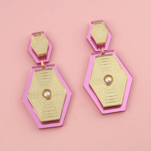 Hexagonal pink and gold earrings on a pink background