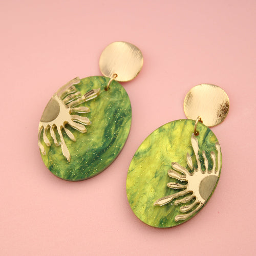 Green earrings with gold accents on a pink background