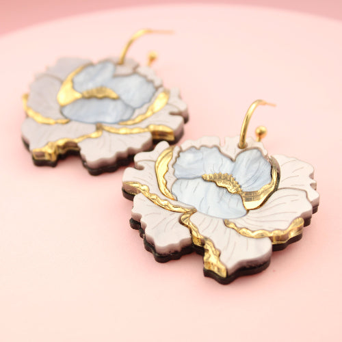 Pair of floral earrings with gold accents on a pink background