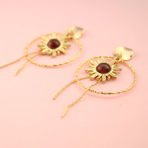 Gold earrings with sunflower design on a pink background