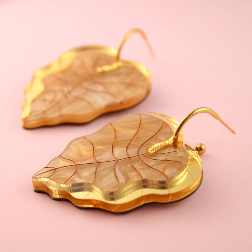 Gold leaf-shaped earrings on a pink background