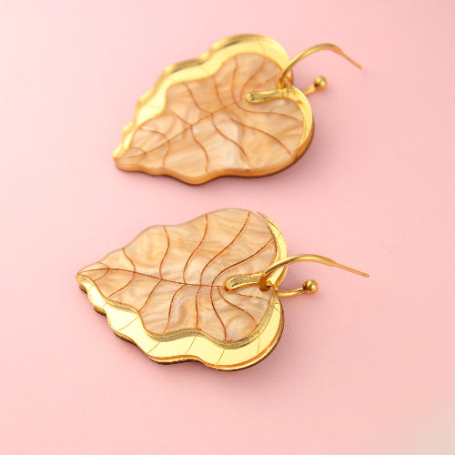 Gold leaf-shaped earrings on a pink background