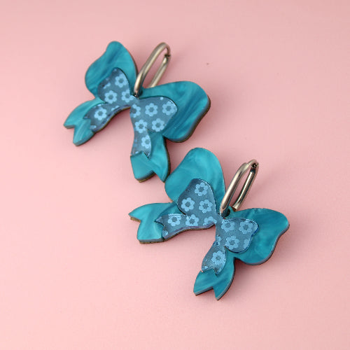 Pair of blue bow-shaped earrings on a pink background