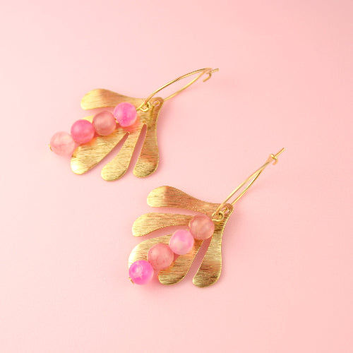 Gold earrings with pink beads on a pink background