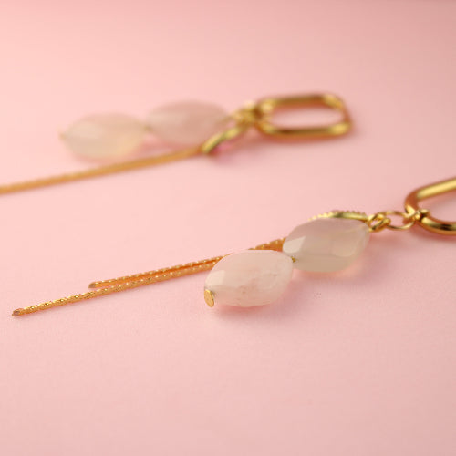 Gold earrings with pink stones on a pink background