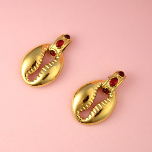 Gold shell-shaped earrings with red stones on a pink background