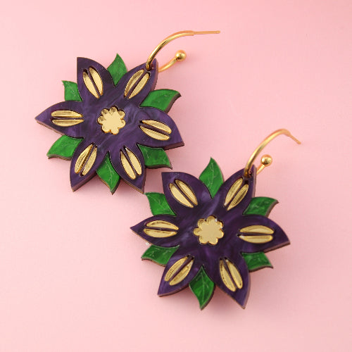 Floral earrings with purple, green, and gold colors on a pink background