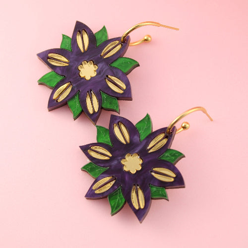 Floral earrings with purple, green, and gold colors on a pink background