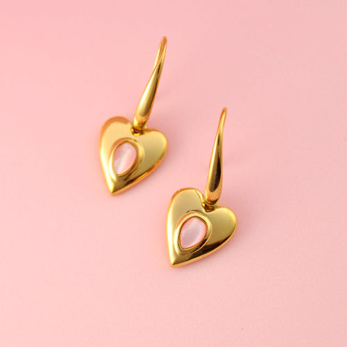 Gold heart-shaped earrings on a pink background