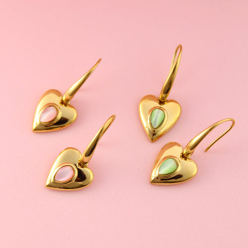 Set of gold heart-shaped earrings with gemstones on a pink background