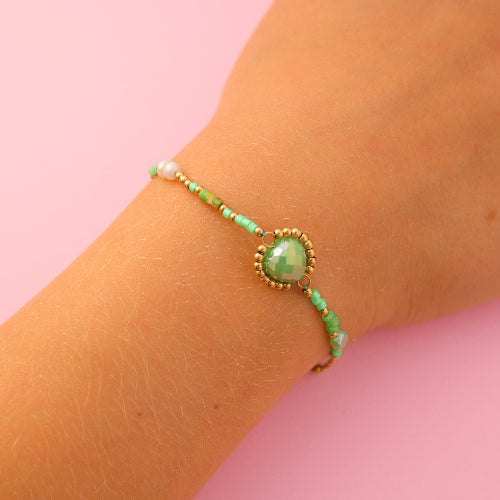 Green beaded bracelet on a wrist against a pink background