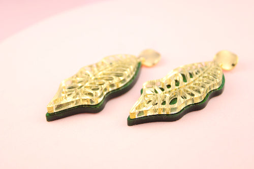 Gold leaf-shaped earrings on a pink background