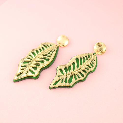 Green leaf-shaped earrings on a pink background
