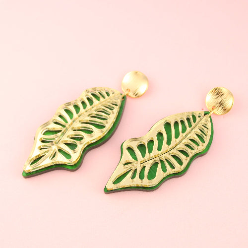 Green leaf-shaped earrings on a pink background