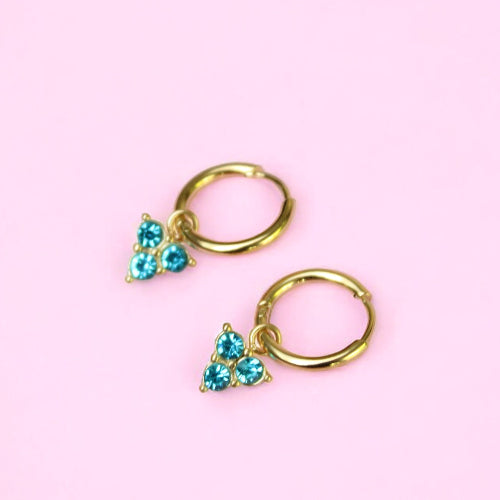 Gold hoop earrings with turquoise stones on a pink background