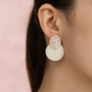 Close-up of a person wearing a white earring  on a pink background