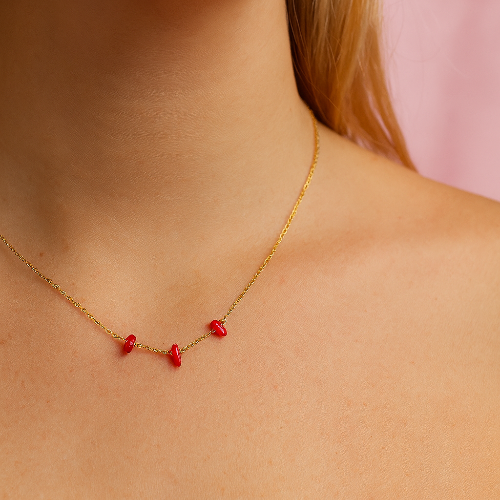 Gold necklace with red stones worn by a person against a pink background