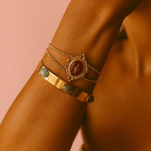 Close-up of a person's arm wearing multiple gold bracelets on a pink background