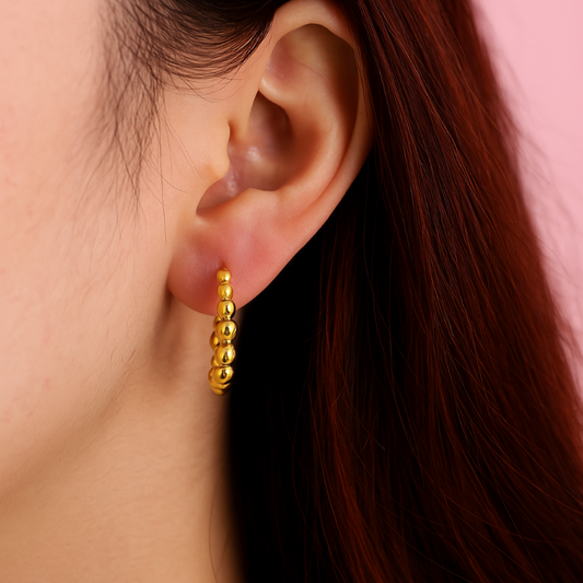 Gold hoop earring worn by a person with red hair against a pink background