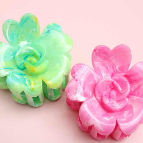 Two colorful flower-shaped hair clips on a pink background