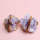 Pair of purple floral earrings with gold accents on a pink background