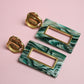 Marble-patterned earrings with gold accents on a pink background