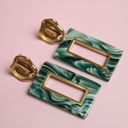 Marble-patterned earrings with gold accents on a pink background