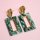 Green marbleized earrings with gold accents on a pink background