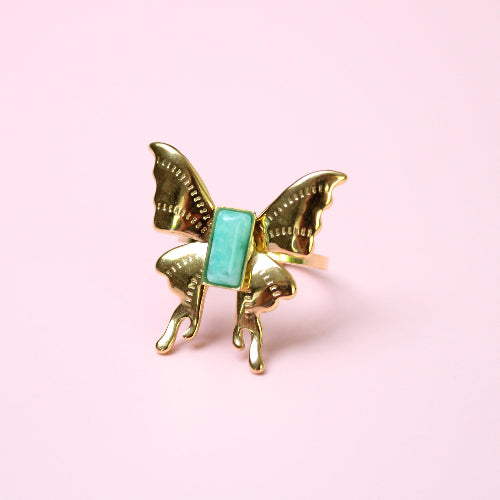 Gold butterfly ring  with a turquoise center on a pink background