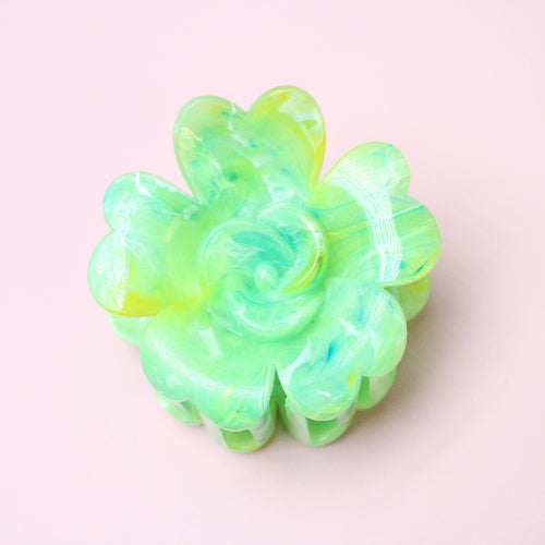 Green flower-shaped hair clip on a light pink background