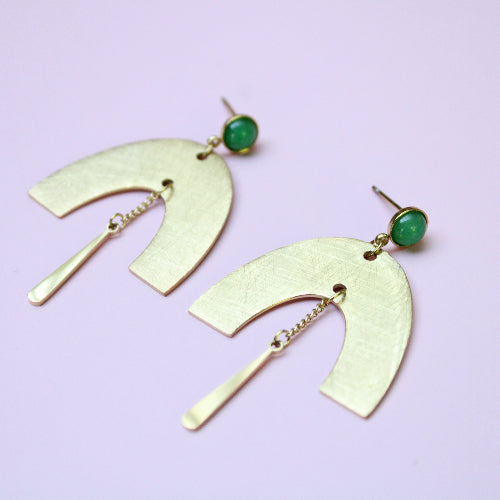 Gold earrings with green gemstones on a light purple background