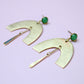 Gold earrings with green gemstones on a light purple background