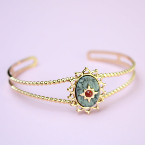 Gold bracelet with a green stone and red gem on a light pink background