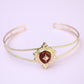 Gold bracelet with a red gemstone on a light purple background