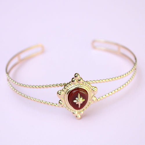 Gold bracelet with a red gemstone on a light purple background