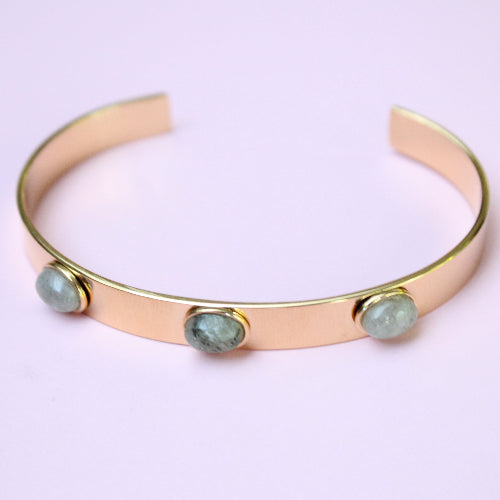 Gold bracelet with three green gemstones on a light purple background