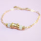 Gold bracelet with green beads on a light pink background