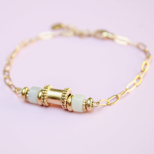 Gold bracelet with green beads on a light pink background